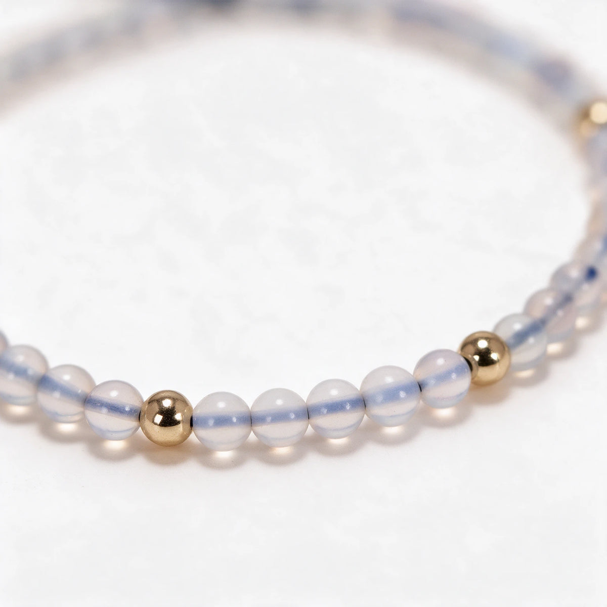 Zbliżenie mlecznych koralików z opalu i kuleczki w złotym kolorze, bransoletka Tessia