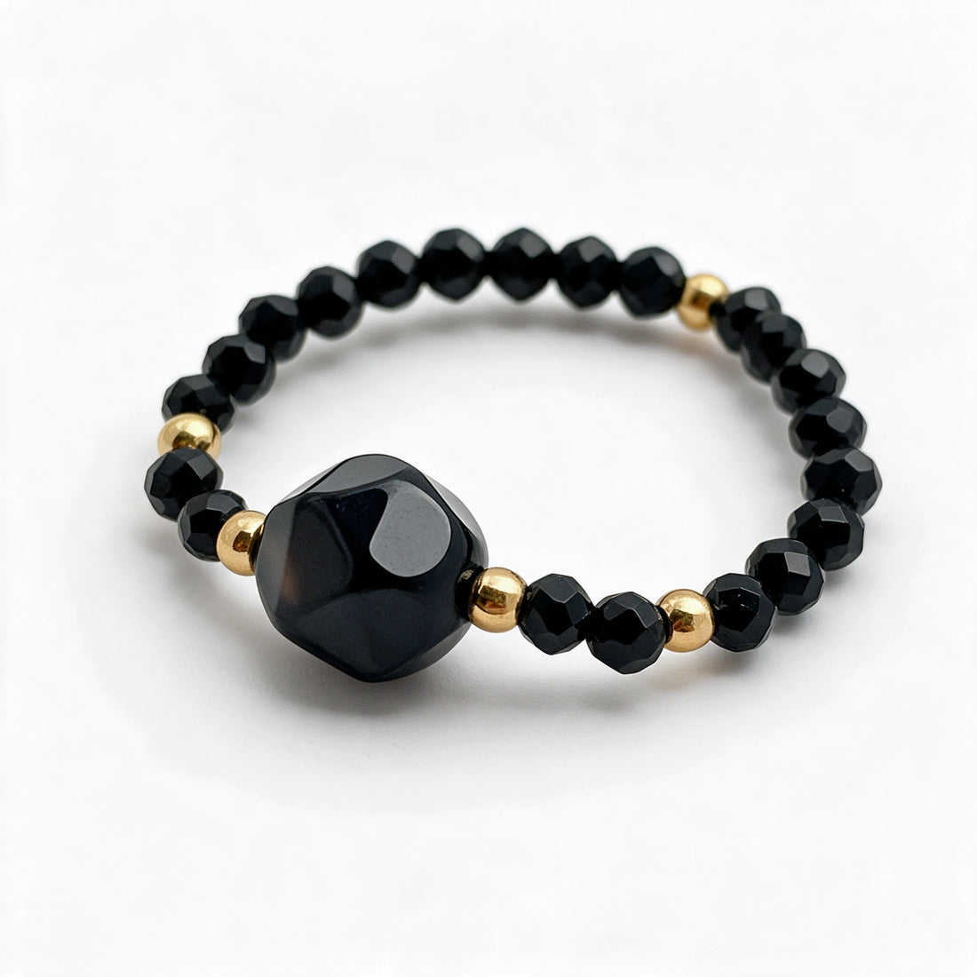 Nolia Obsydian, jeden pierścionek z fasetowanych koralików na jasnym tle.