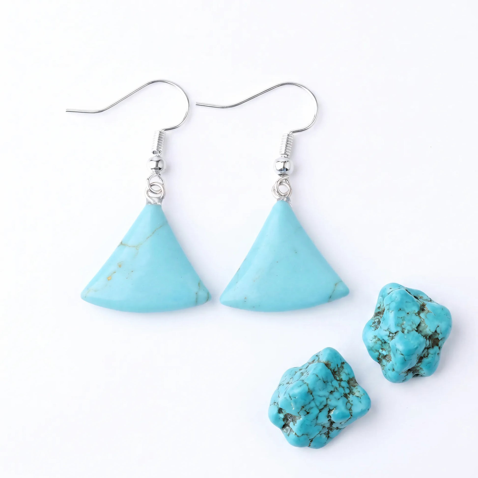 Trójkątne kolczyki z naturalnego turkusu szlachetnego Eos na srebrnych biglach obok surowych bryłek kamienia