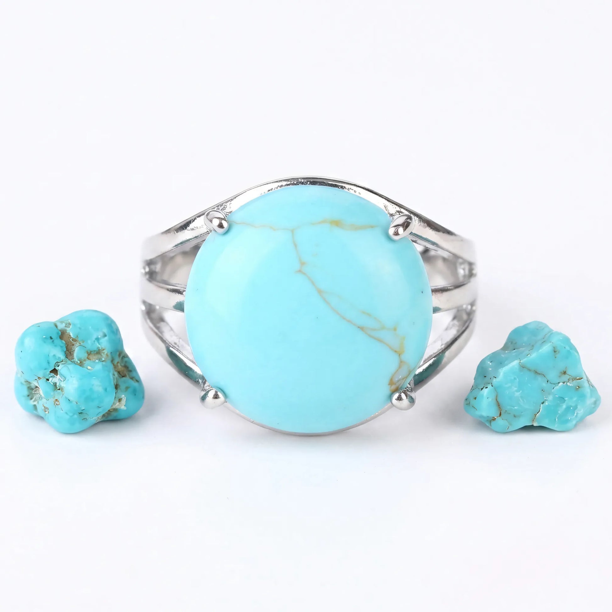 Srebrny pierścionek z dużym błękitnym naturalnym turkusem Veda obok surowych kamieni na białym tle